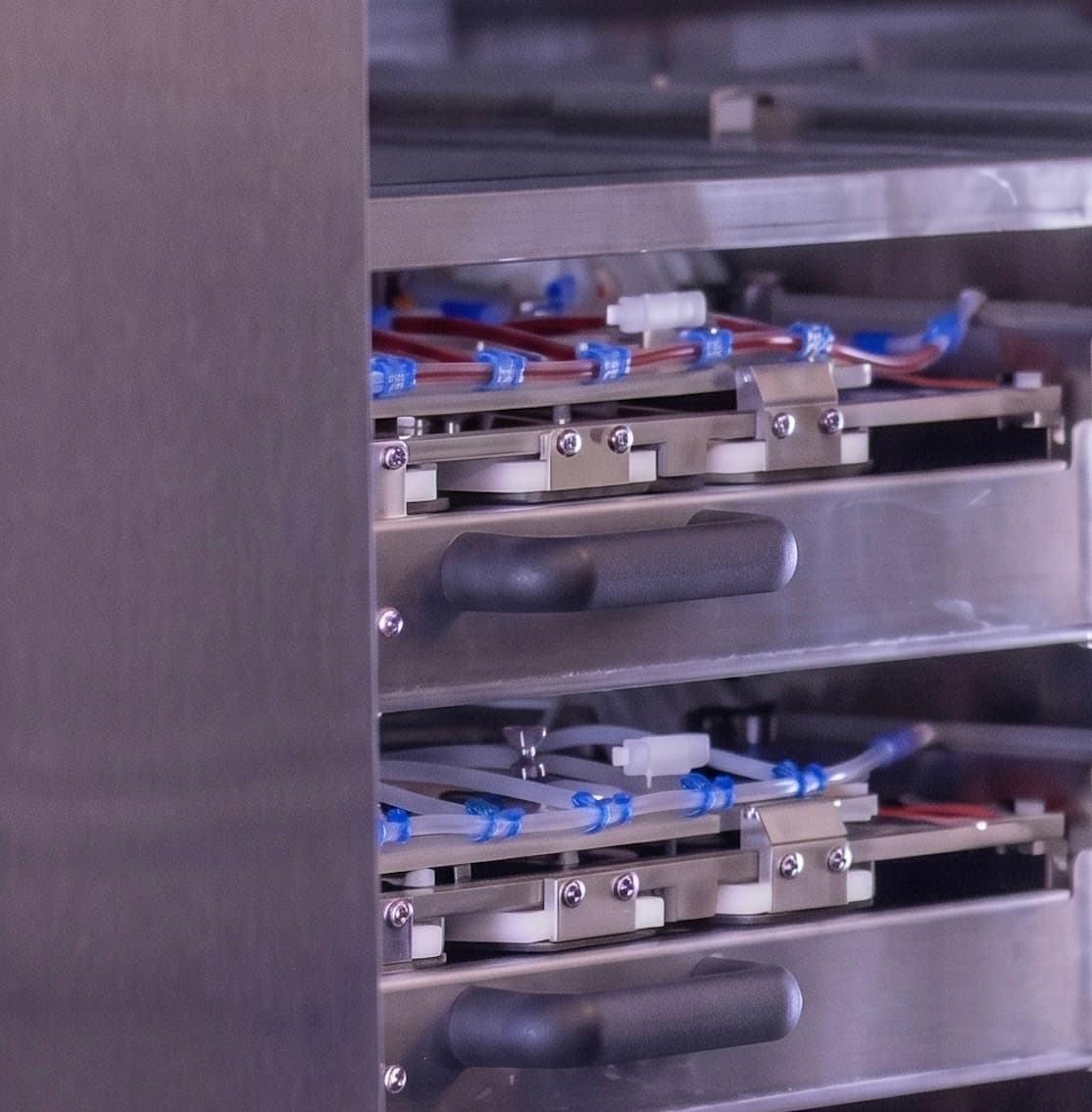 Stacked stainless-steel culture trays inside the pulsatile bioreactor, with tubing that circulates conditioning fluid to the growing tissue